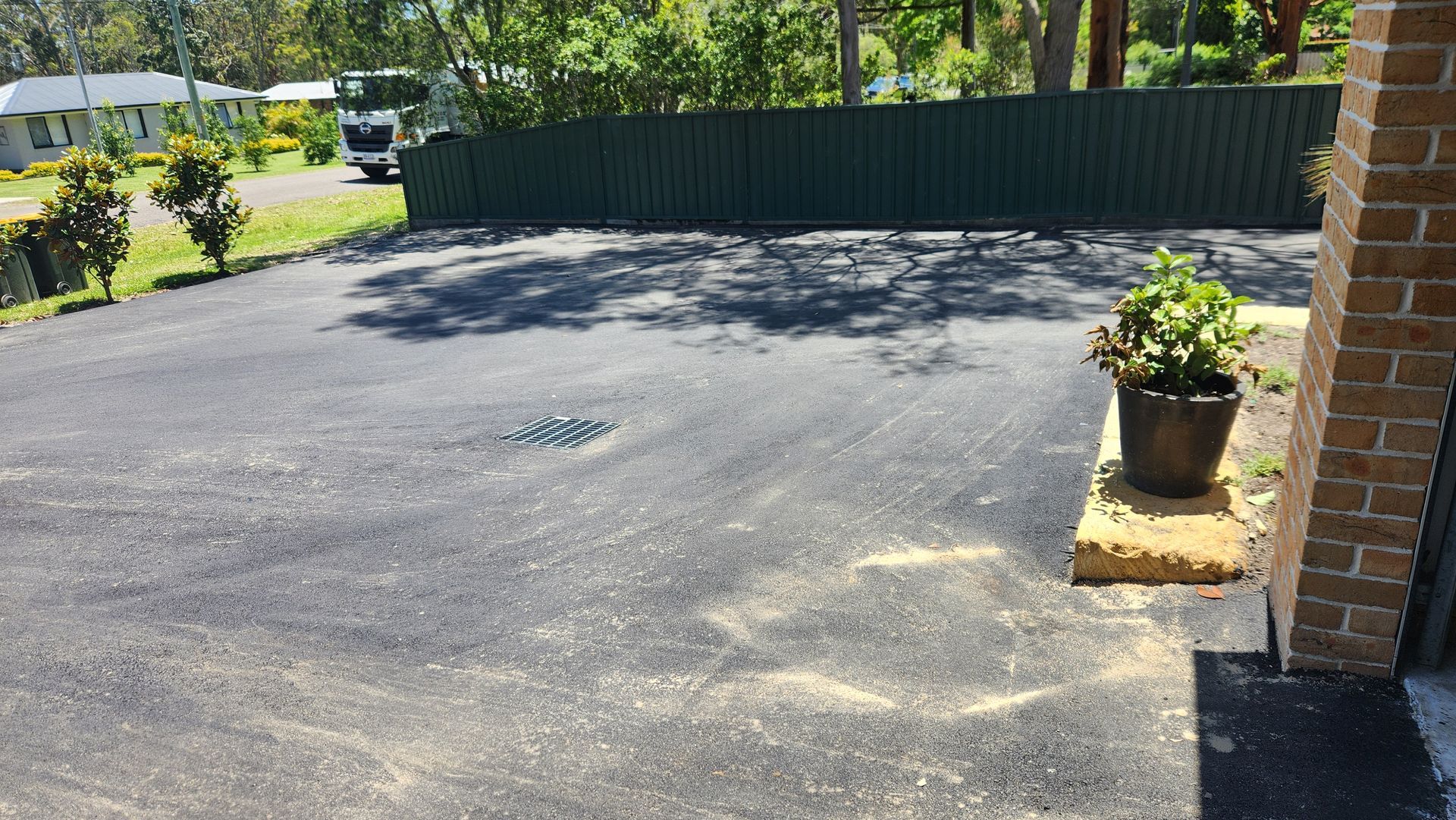 Black Asphalt Driveway With A Green Fence, Trees — TAC Asphalt Services in Warners Bay, NSW