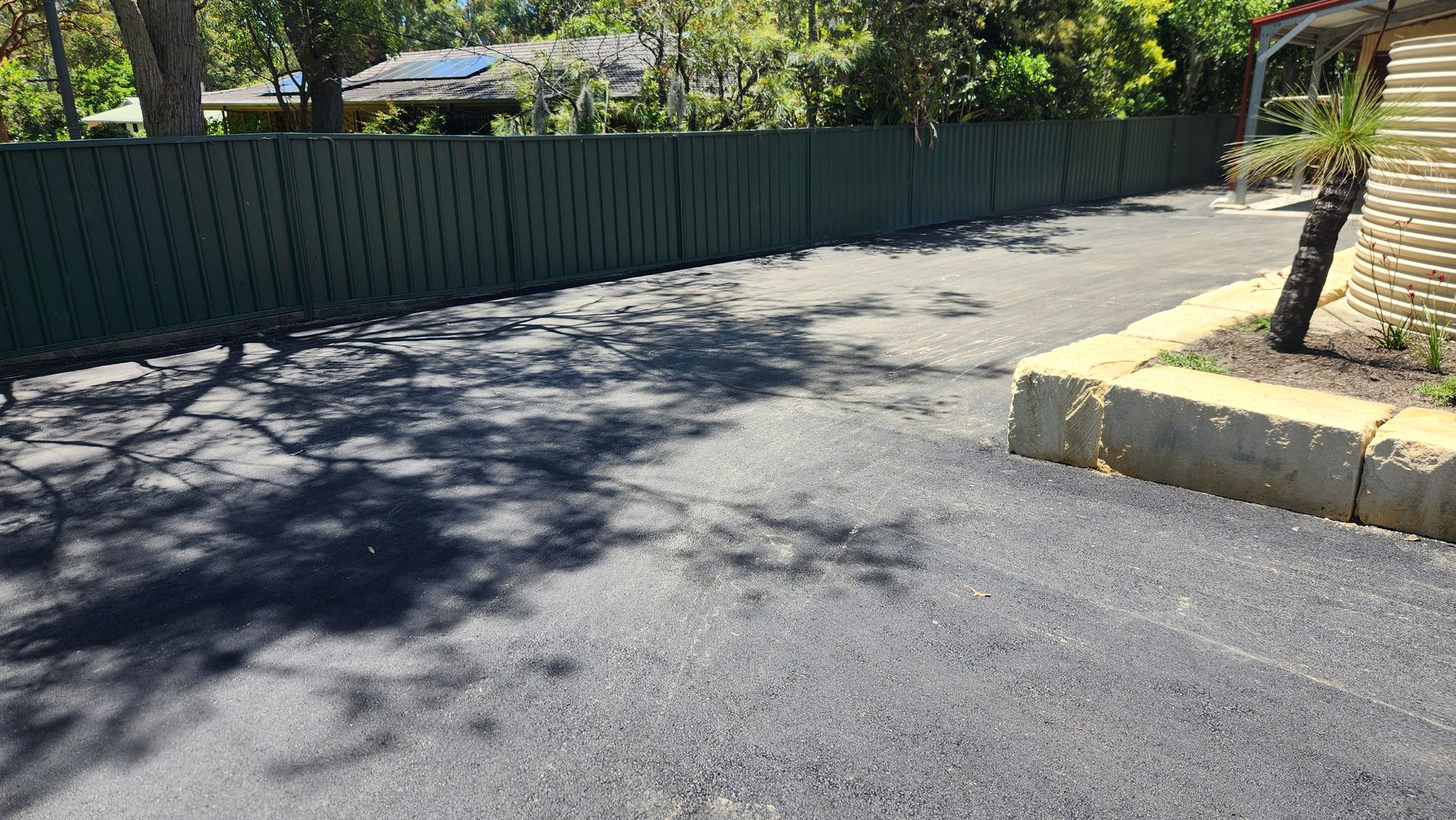Asphalt Driveway With Green Fence, Trees, And Stone Garden Bed — TAC Asphalt Services in Warners Bay, NSW