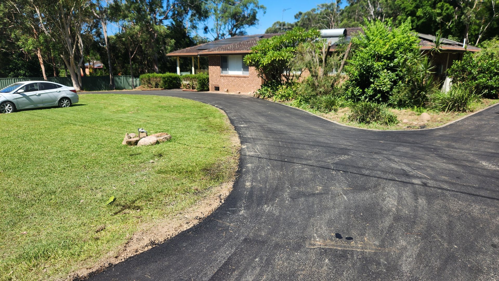 Asphalt Driveway Leading To A Brick House On A Grassy Lawn — TAC Asphalt Services in Warners Bay, NSW