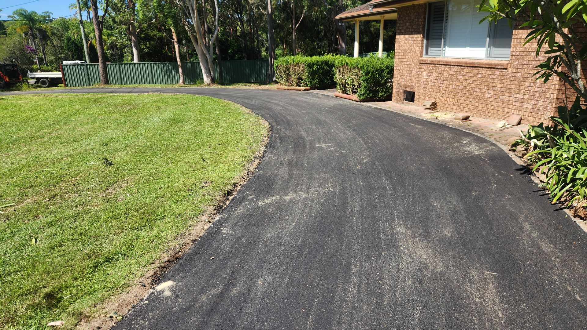Asphalt Driveway Curves Toward A Brick House With Green Lawn — TAC Asphalt Services in Warners Bay, NSW