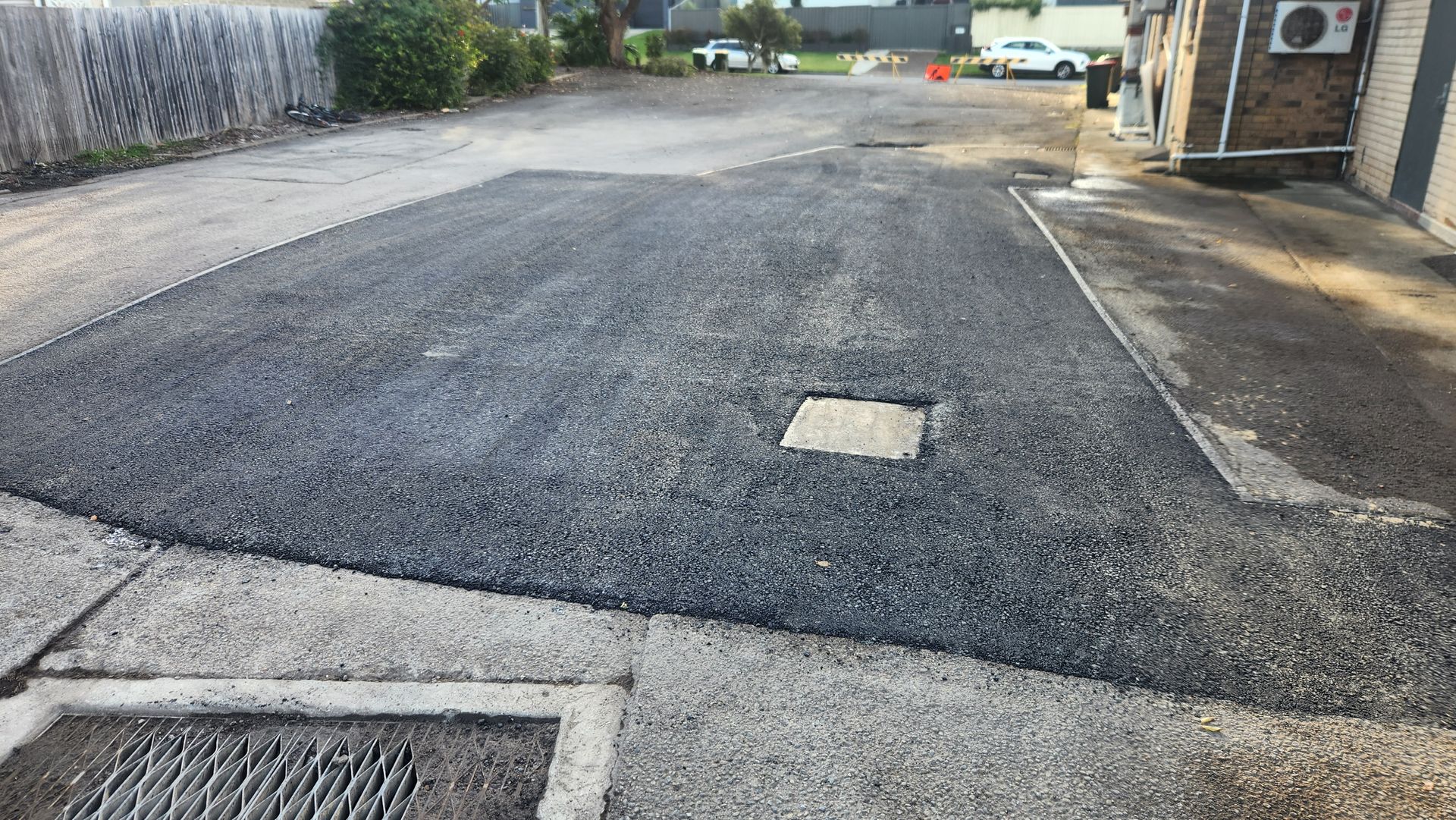A rectangular patch of freshly laid, dark gravel fills a section of a weathered concrete parking lot.