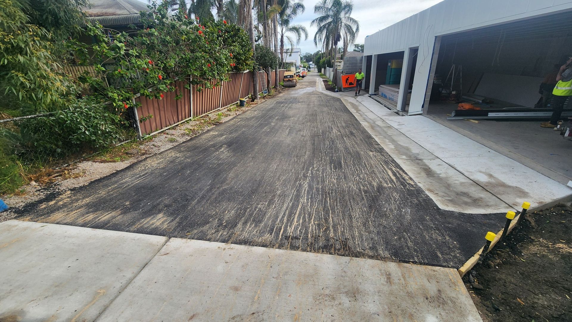 A newly paved gravel driveway leading between a fence and a modern garage building.