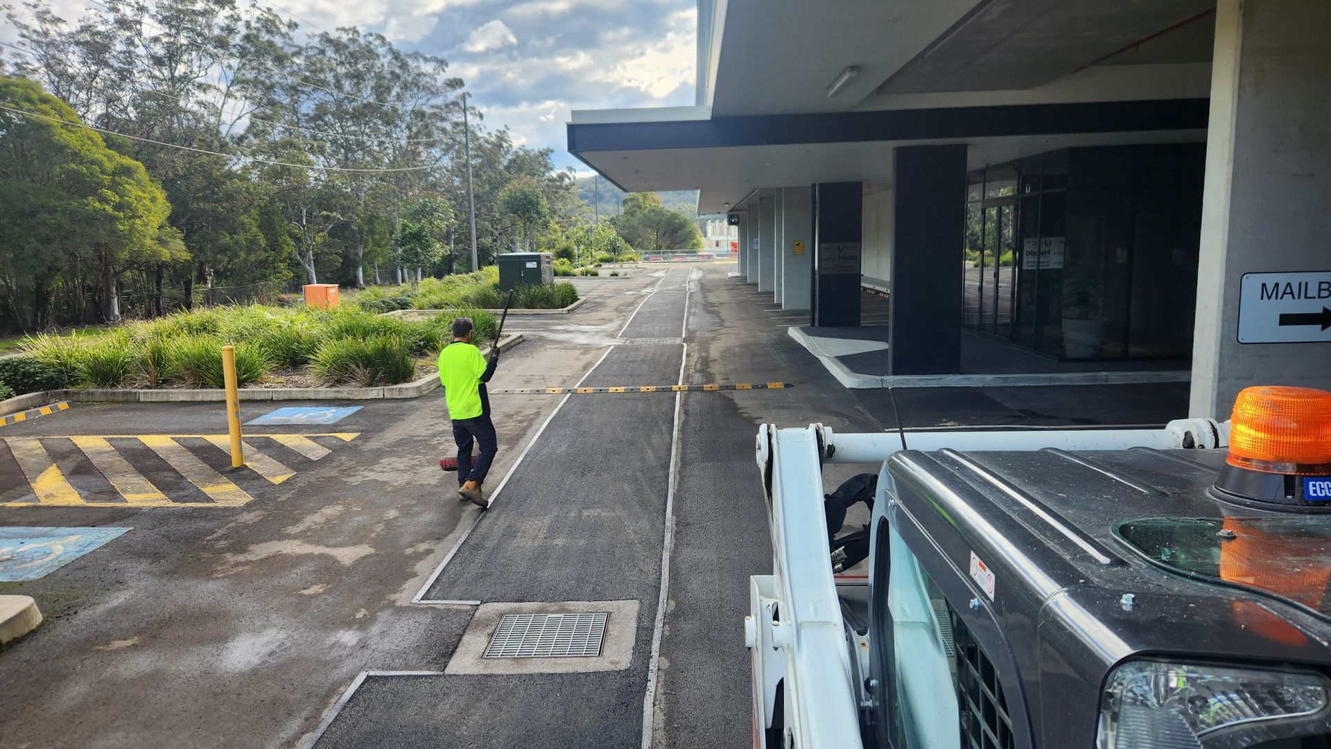 Man in Safety Vest Walks Along a Newly Paved Road Next to a Building — TAC Asphalt Services in Central Coast, NSW