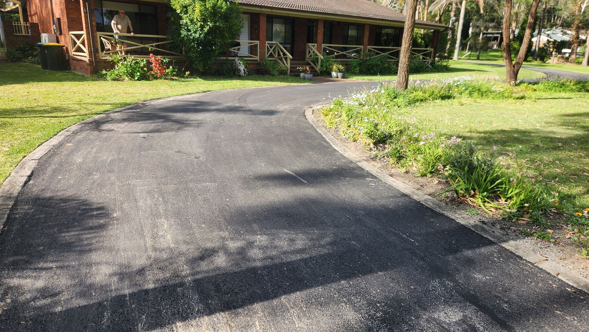 Asphalt Driveway Curves Through A Grassy Lawn Toward A Wooden Building — TAC Asphalt Services in Warners Bay, NSW