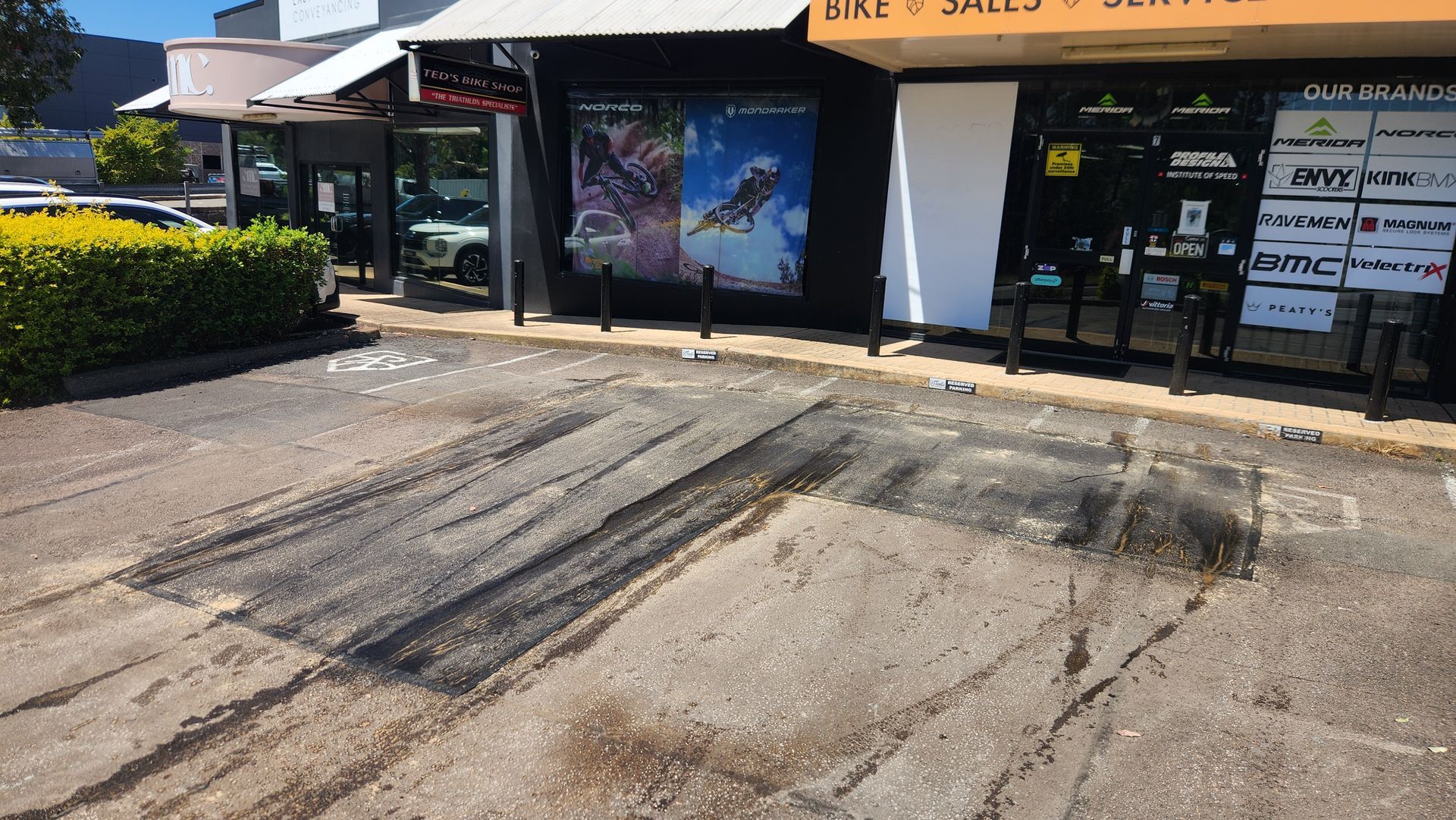 Asphalt With Dark Tire Marks In Front Of Businesses Under A Covered Walkway — TAC Asphalt Services in Warners Bay, NSW