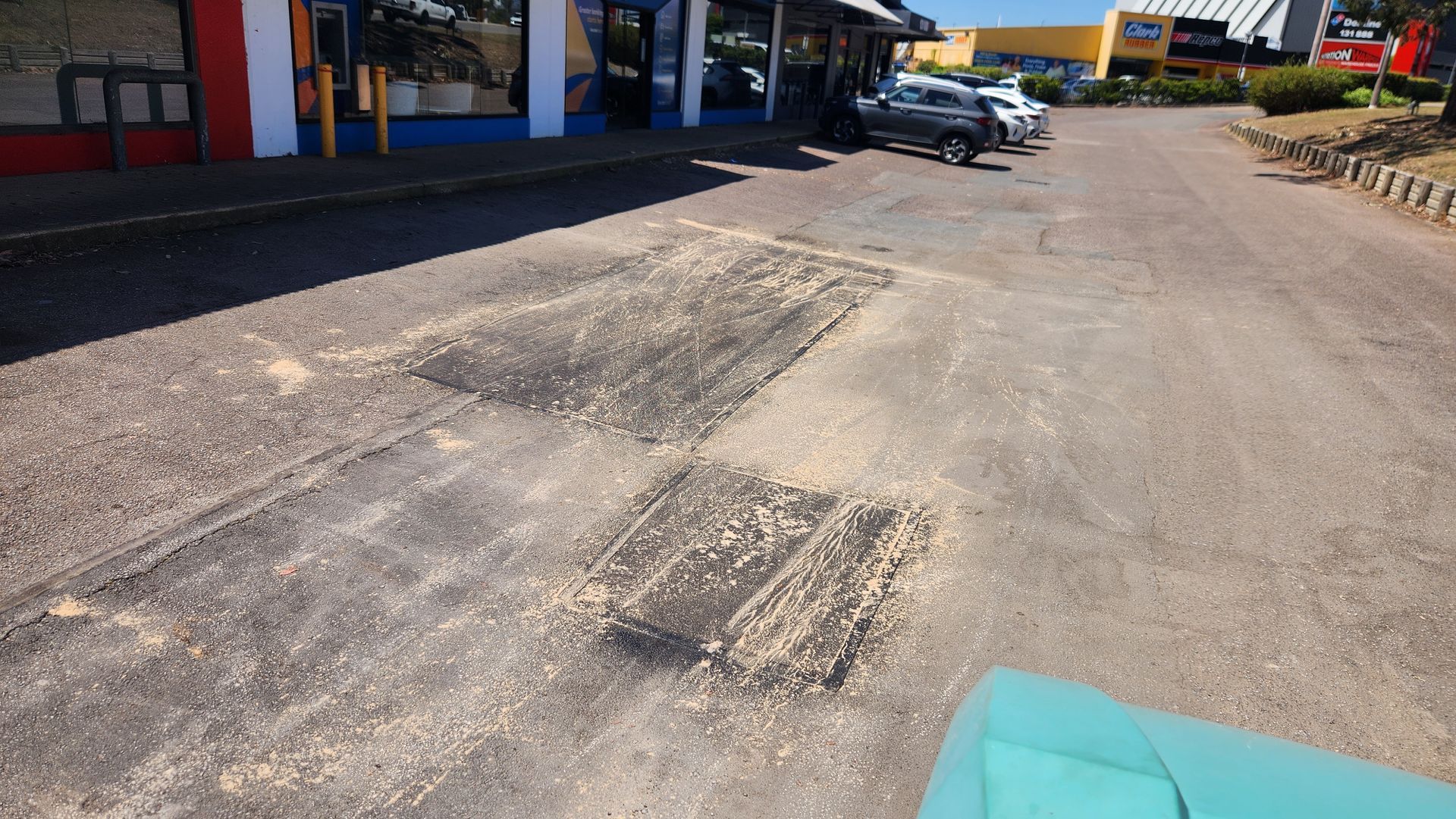 Damaged Asphalt With Rectangular Patches And Building In The Background — TAC Asphalt Services in Warners Bay, NSW