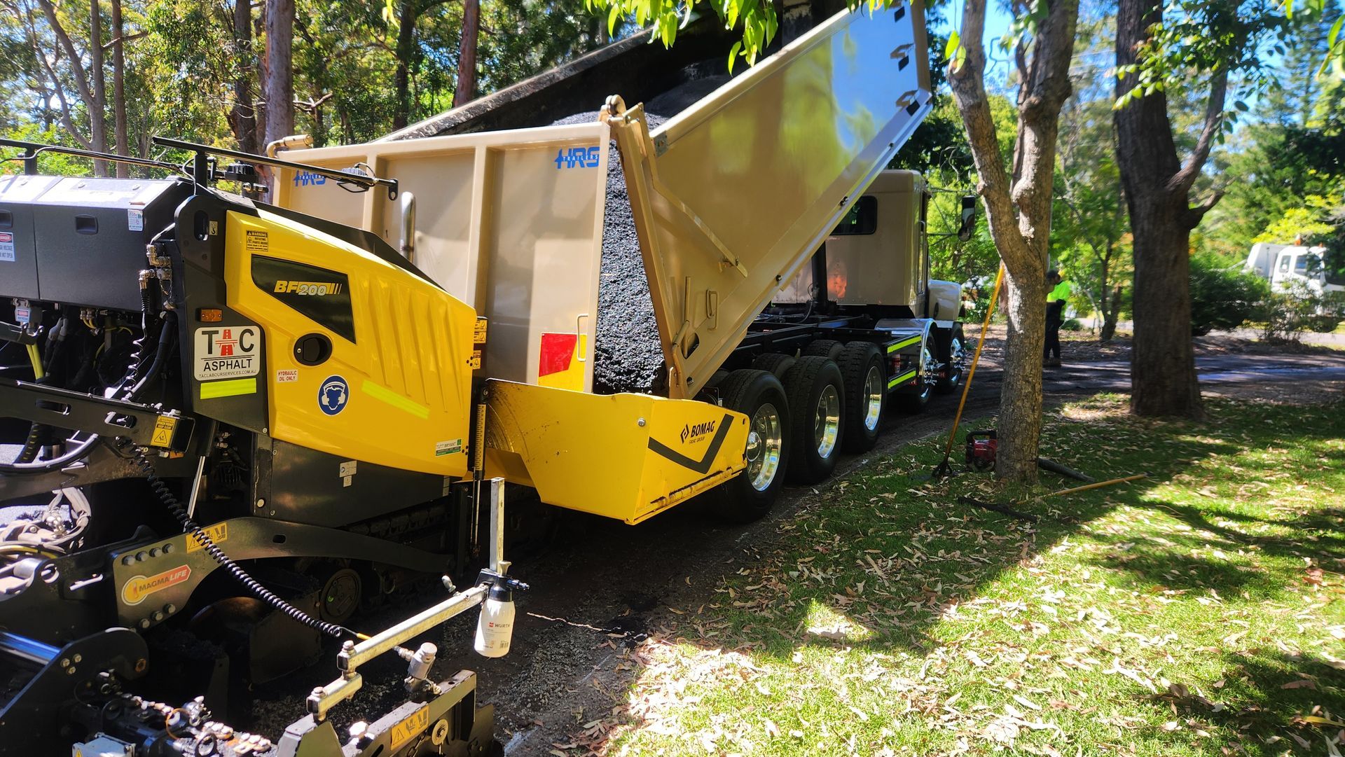 Yellow Asphalt Paving Machine Receiving Asphalt From A Dump Truck — TAC Asphalt Services in Warners Bay, NSW
