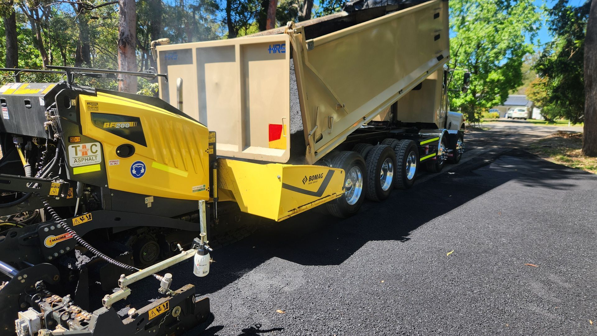Yellow Paver Receiving Asphalt From a Dump Truck on a Street — TAC Asphalt Services in Warners Bay, NSW
