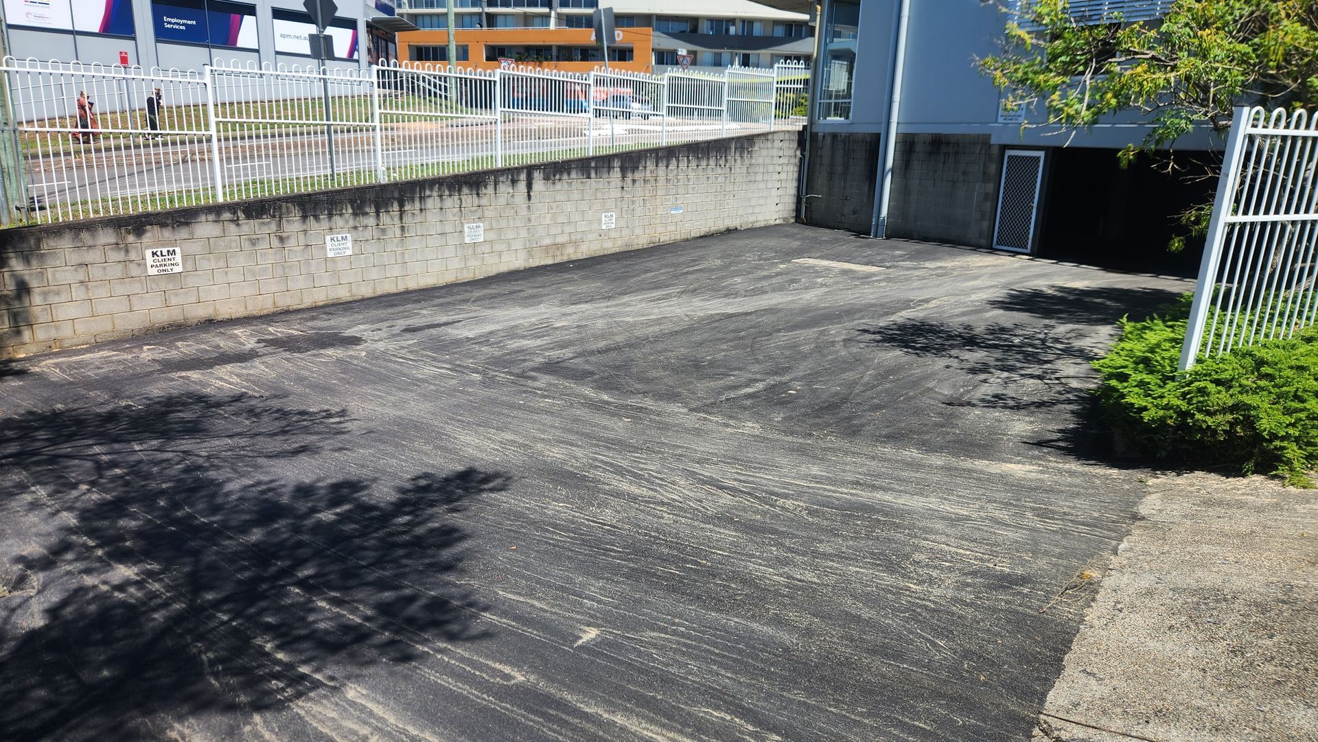 Asphalt Parking Area With Worn Surface, Bordered by Concrete Walls and a Fence — TAC Asphalt Services in Hunter Valley, NSW