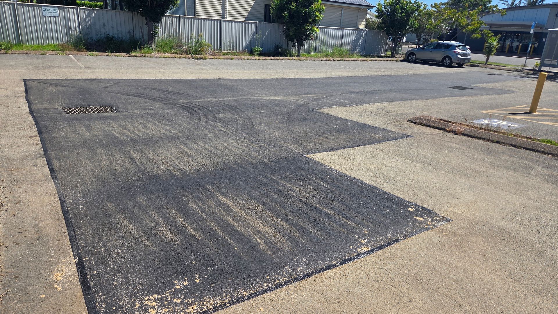 Patch of New Asphalt on a Parking Lot. Grey Cars and a Fence in the Background — TAC Asphalt Services in Central Coast, NSW