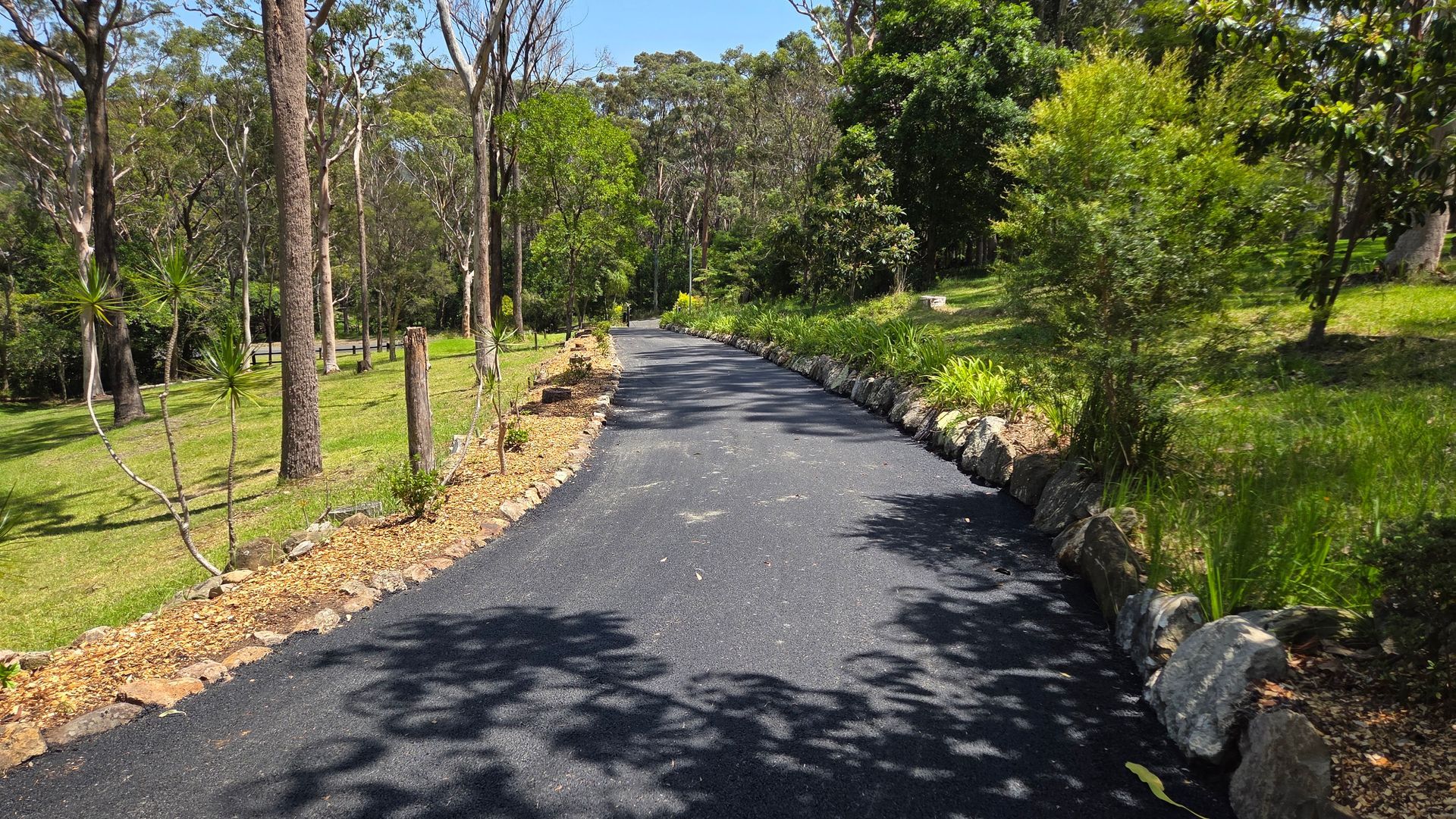 Asphalt Driveway Curves Through a Wooded Area With Trees And Grass — TAC Asphalt Services in Port Stephens, NSW