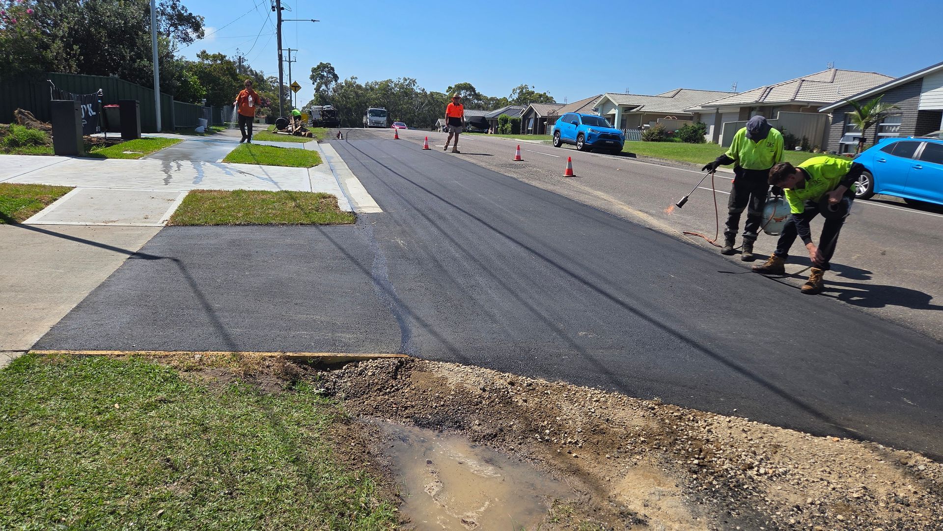 Road Crew Paving a Street. Fresh Black Asphalt, Orange Cones, Sunny Day — TAC Asphalt Services in Warners Bay, NSW
