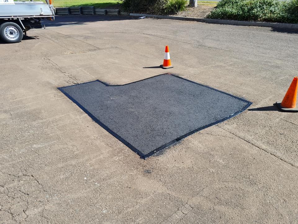 Asphalt Patch on a Paved Surface, Two Orange Traffic Cones Are Set Up — TAC Asphalt Services in Warners Bay, NSW