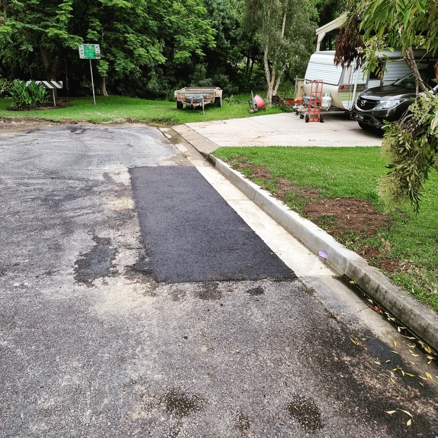 Patch of Fresh Asphalt on Cracked Road Next to a Curb and Grassy Area — TAC Asphalt Services in Warners Bay, NSW