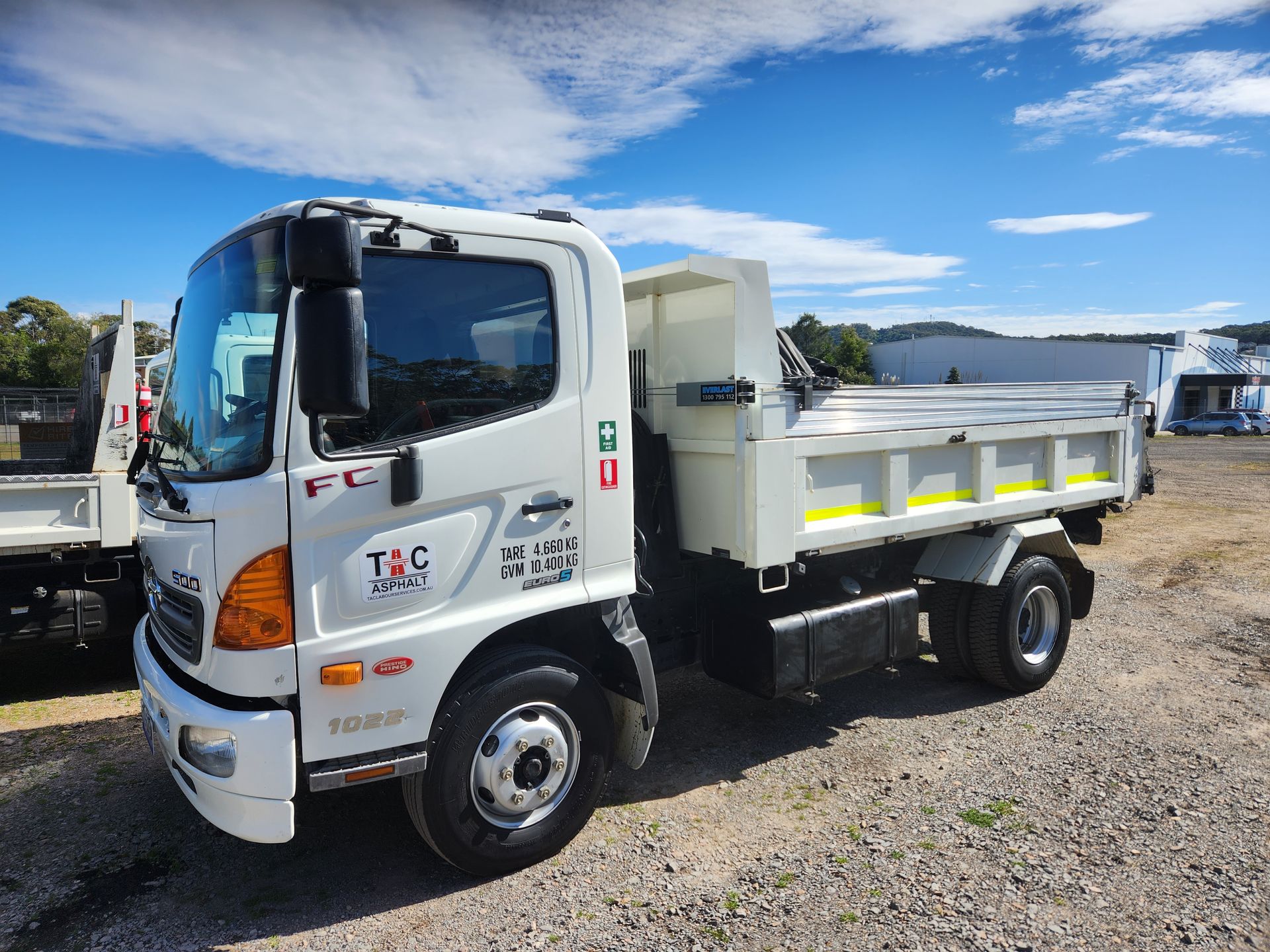 A white Hino dump truck parked on a gravel lot under a blue sky with light clouds.