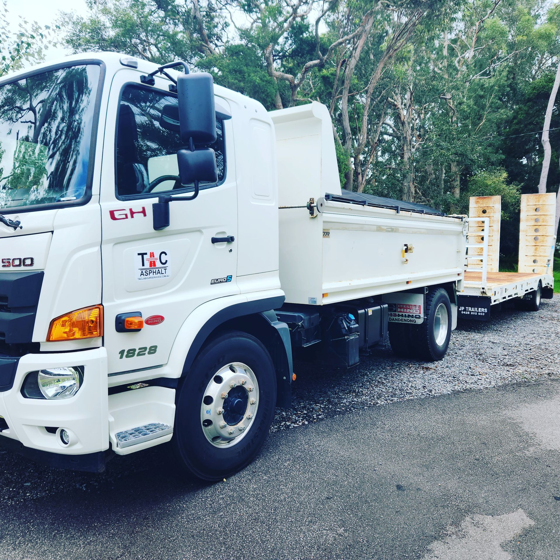 White Hino 1928 dump truck with T&C Transport branding, hitched to a flatbed trailer on a gravel surface.