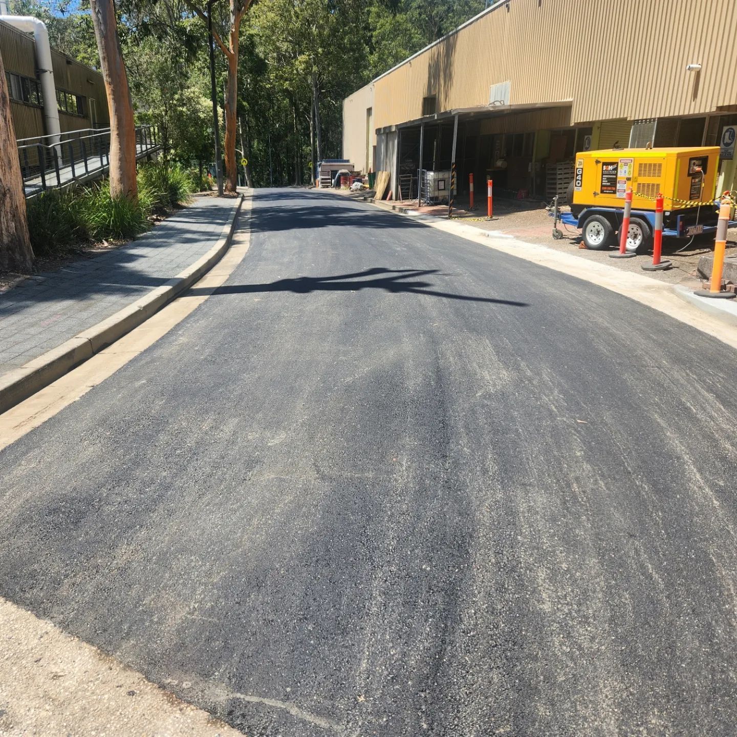 Newly Paved Asphalt Road Next to a Building. Yellow Generator Visible — TAC Asphalt Services in Raymond Terrace, NSW