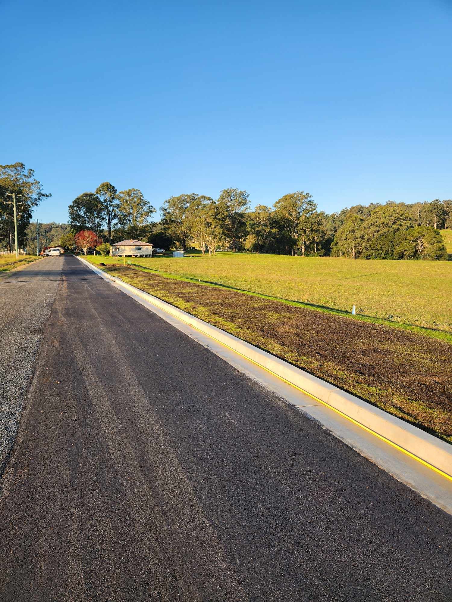 Asphalt Road Next To A Grassy Field — TAC Asphalt Services in Warners Bay, NSW