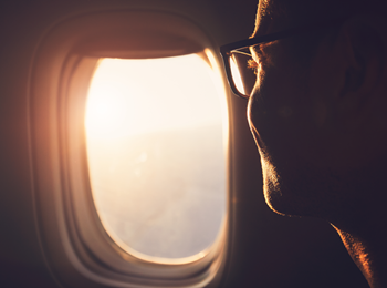 A man wearing glasses is looking out of an airplane window.