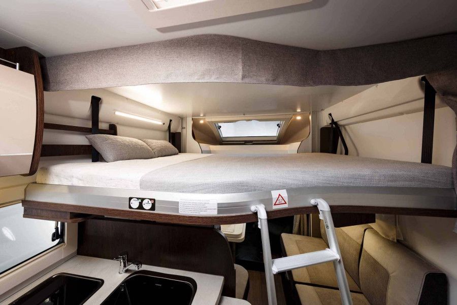 Interieur van een camper, met een bovenbed, ladder, wastafel en zithoek.