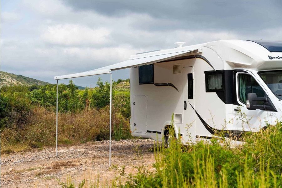 Witte camper met uitgeschoven luifel, geparkeerd tussen de begroeiing op een bewolkte dag.