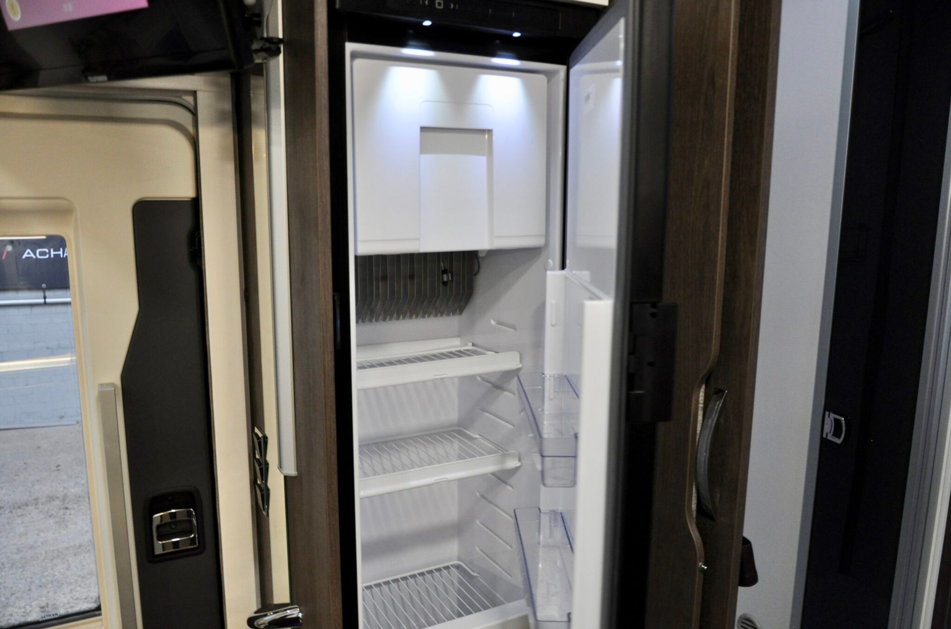 Een open koelkast in een camper, met zichtbare schappen en binnenverlichting.