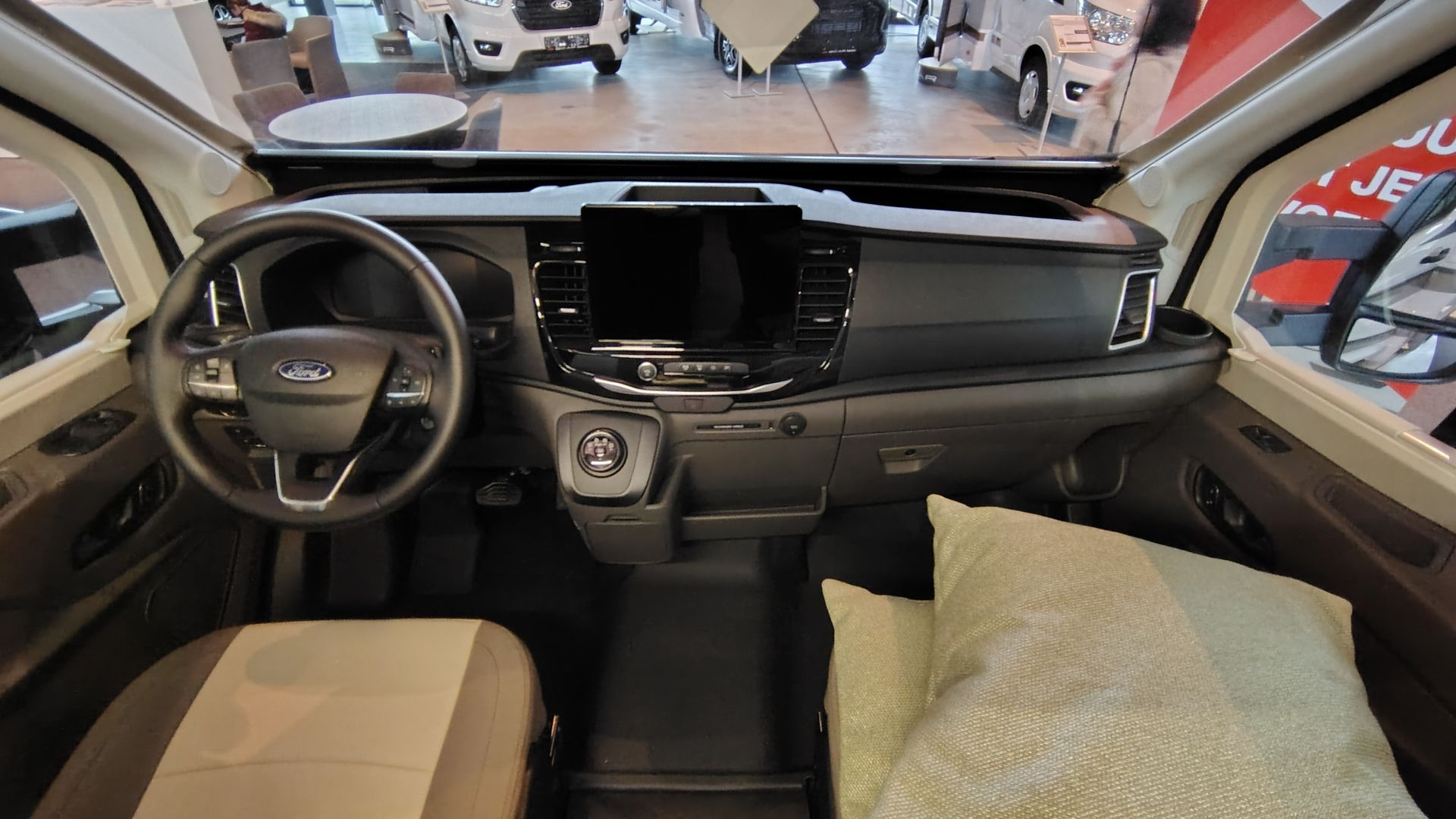 Interieurbeeld van het dashboard van een bestelwagen. Stuurwiel, middenconsole met scherm en een kussen op een stoel.