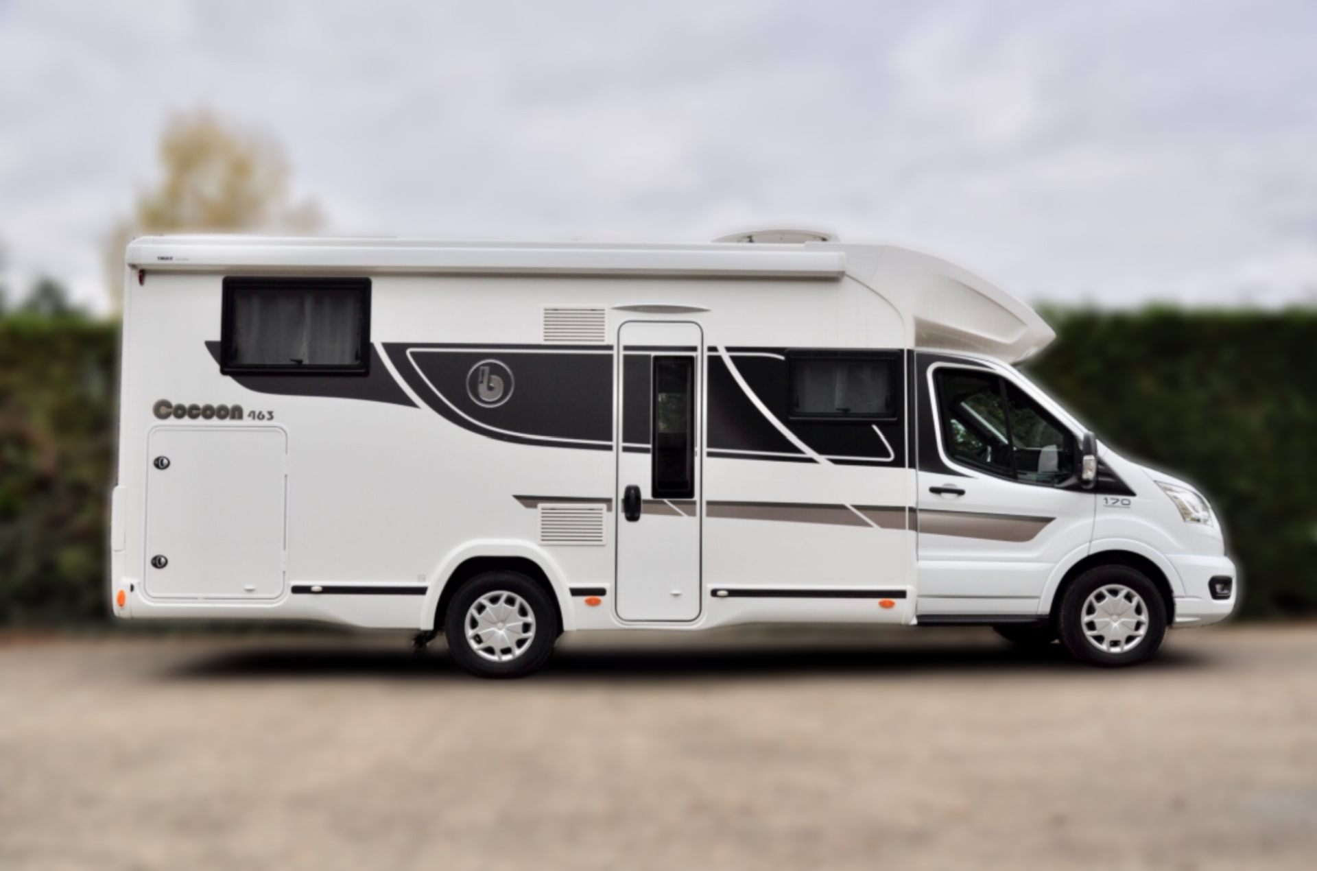 Witte camper geparkeerd op een wazige ondergrond, zijaanzicht, tegen een bewolkte hemel.