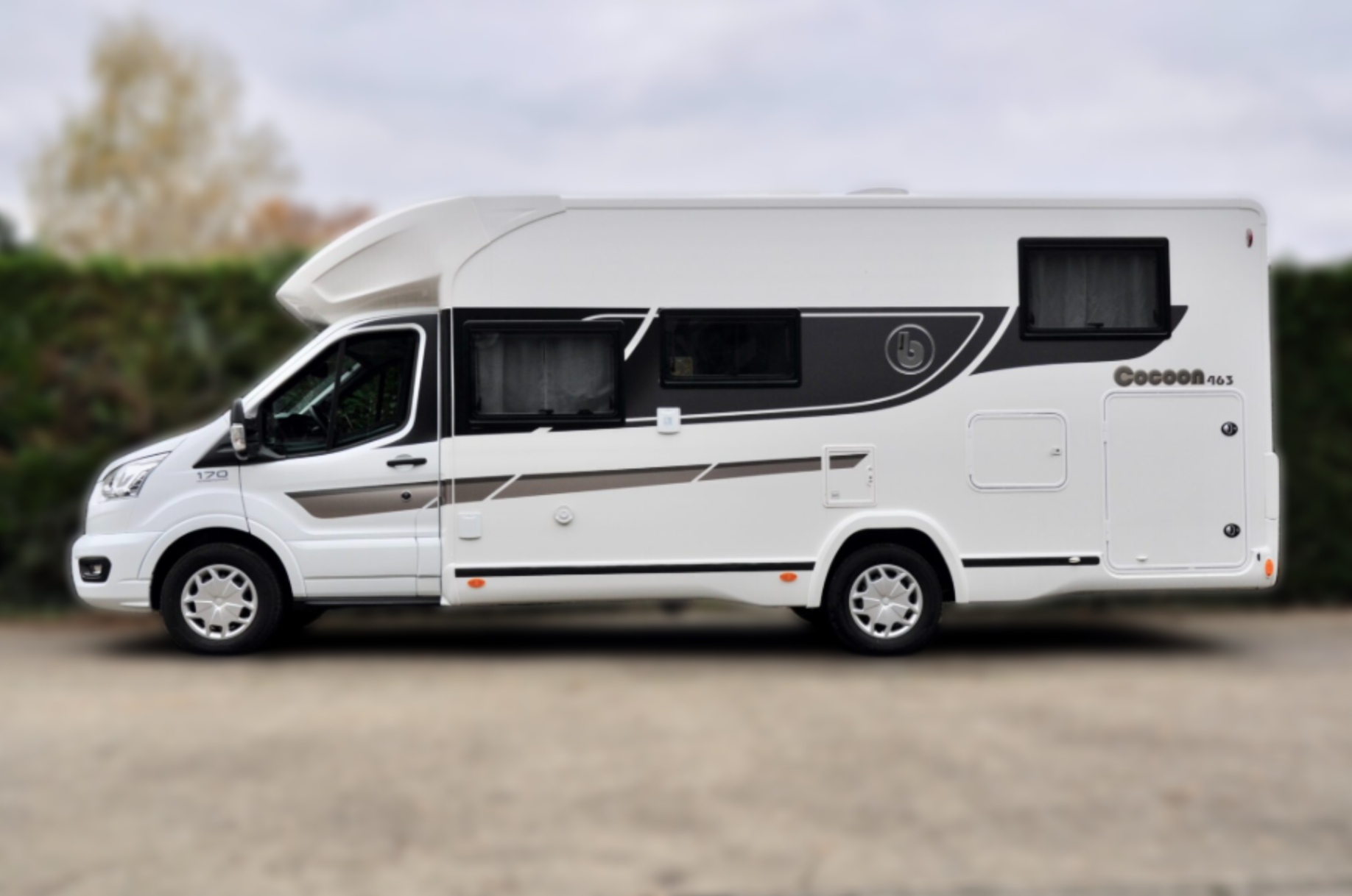 Witte camper geparkeerd op een verharde ondergrond, zijaanzicht, met decoratieve grijze strepen.