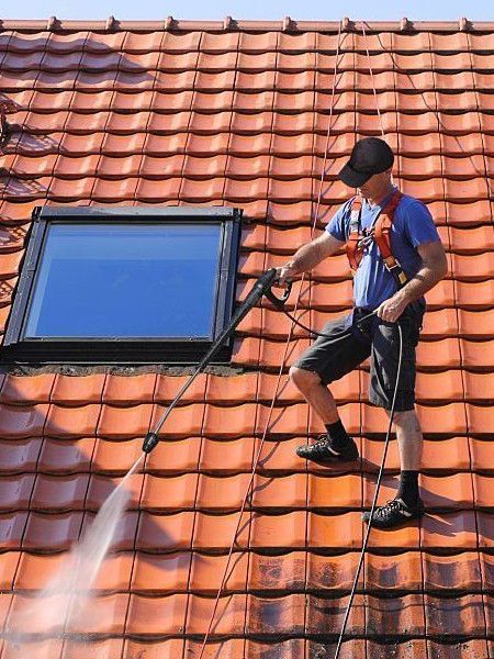 A man is cleaning a tiled roof with a high pressure washer.