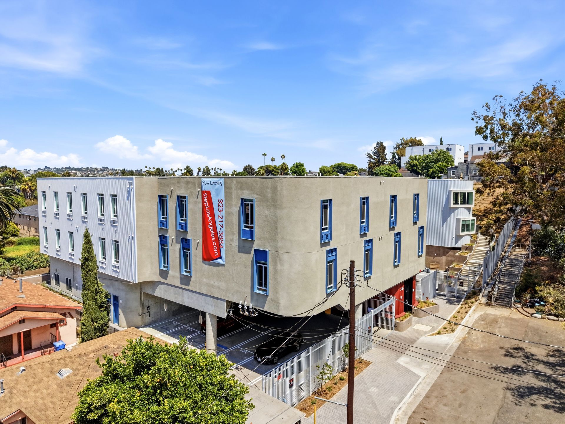 Grey apartment building with blue rectangular windows and red lobby door and surrounding greenery