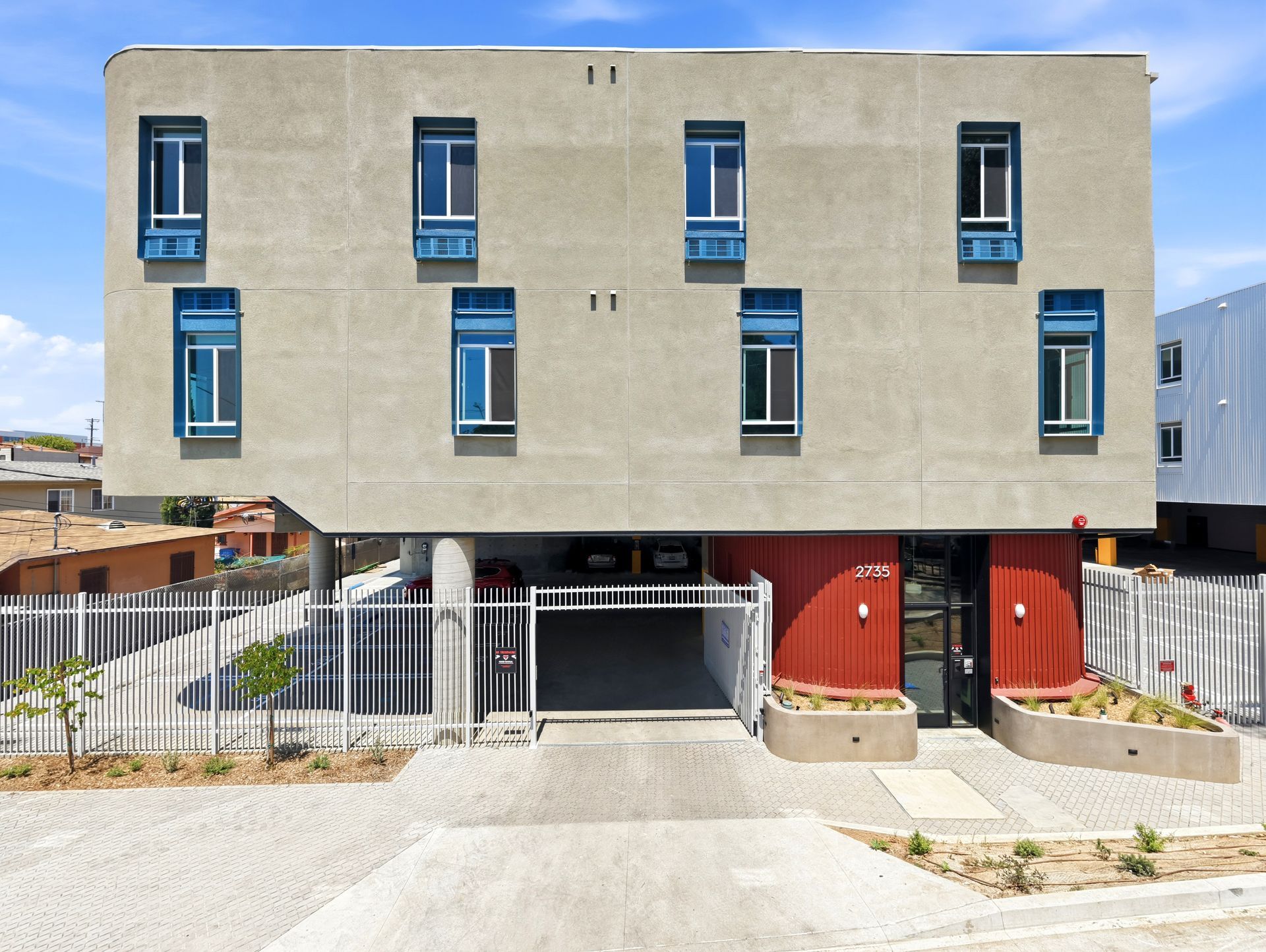 Front of grey apartment building with red lobby door and white garage gate