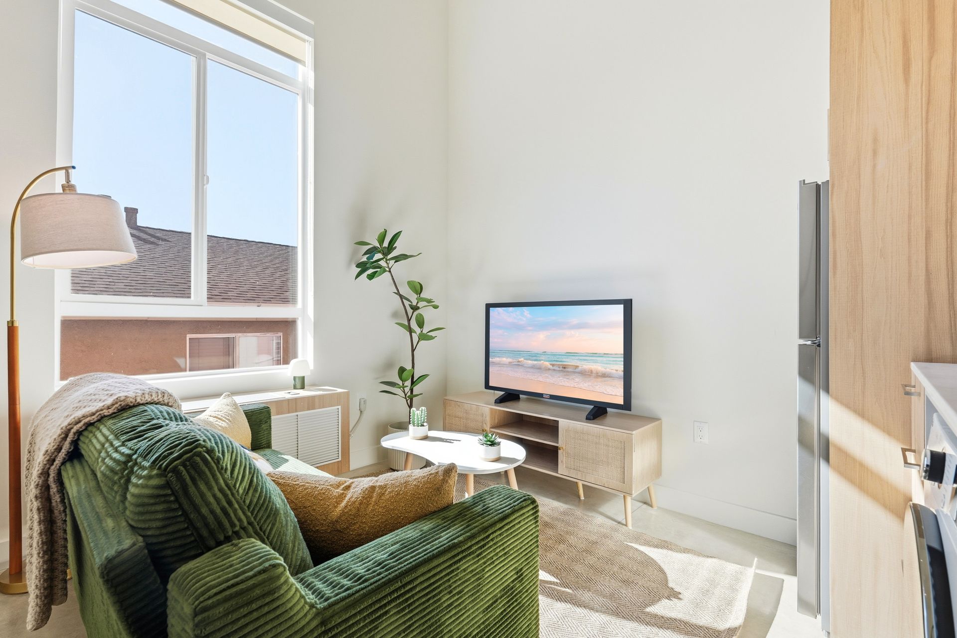 Cozy living room with green corduroy couch, TV, window, and small coffee table.