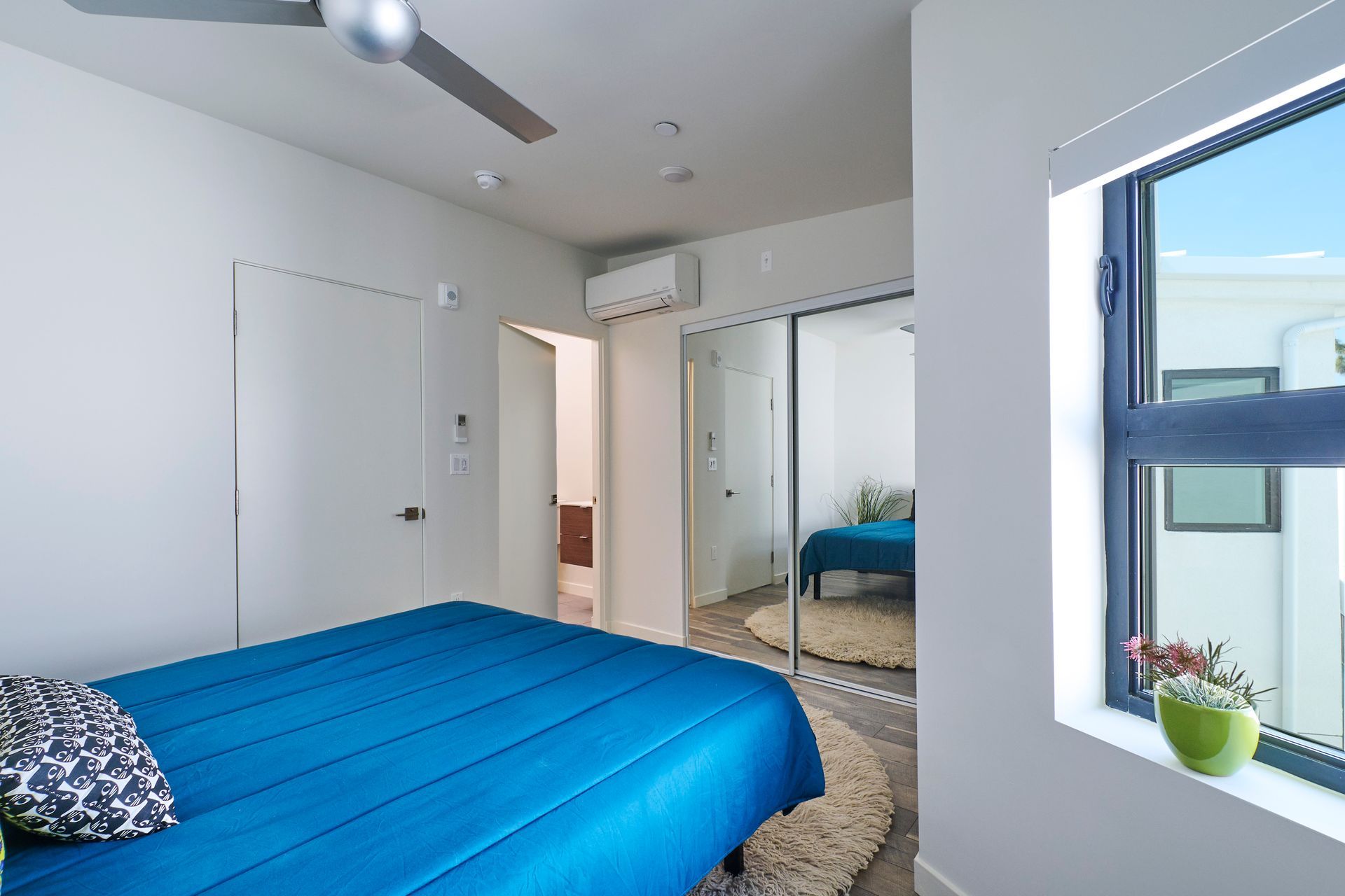 A bedroom with a blue bed , a ceiling fan , and a window.