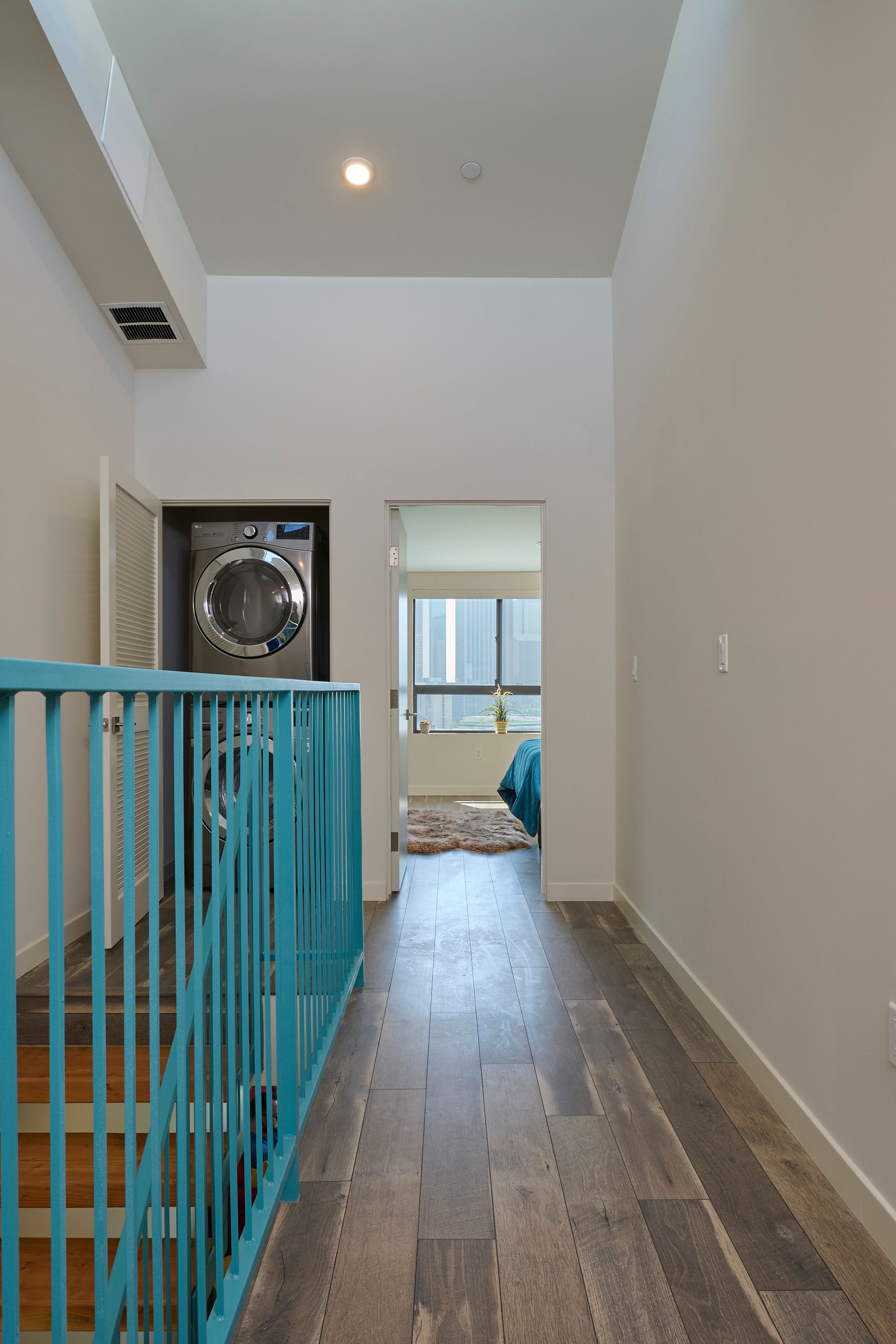 A hallway with a blue railing leading to a laundry room