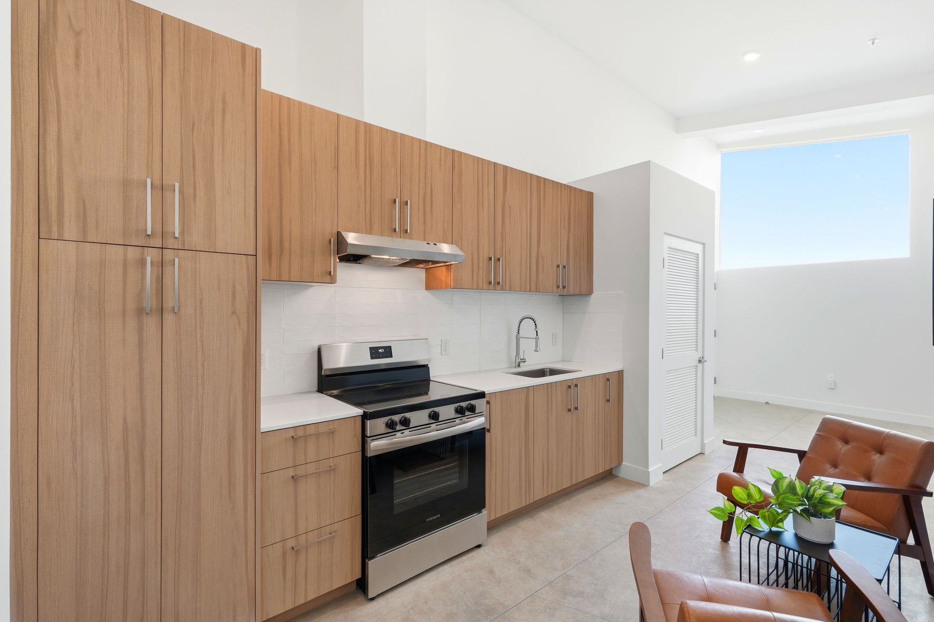 Wooden kitchen cabinets and stainless steel appliances in a bright room with window and chairs.