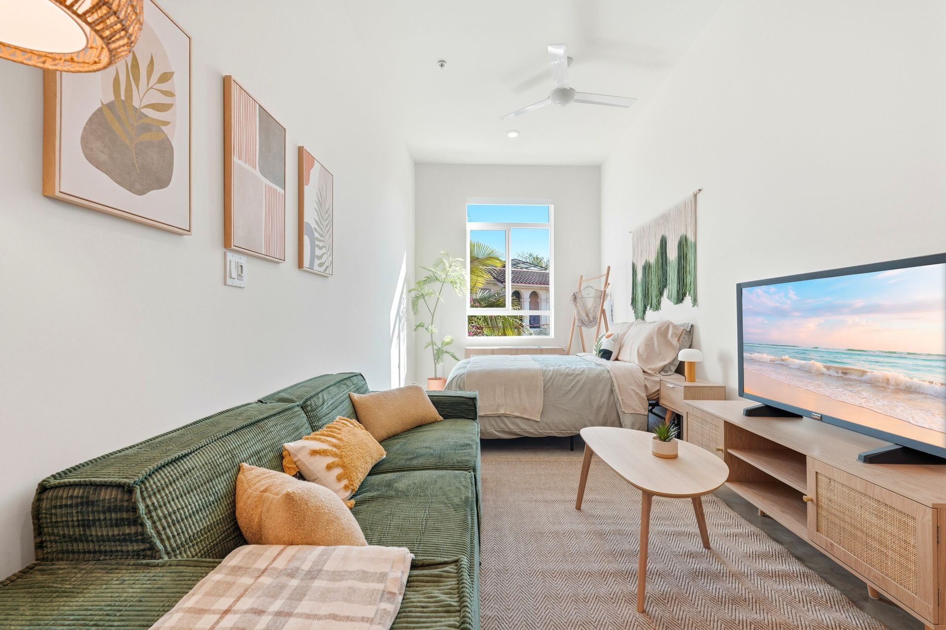 Cozy studio apartment with green sofa, bed, TV, and wall art; bright natural light.