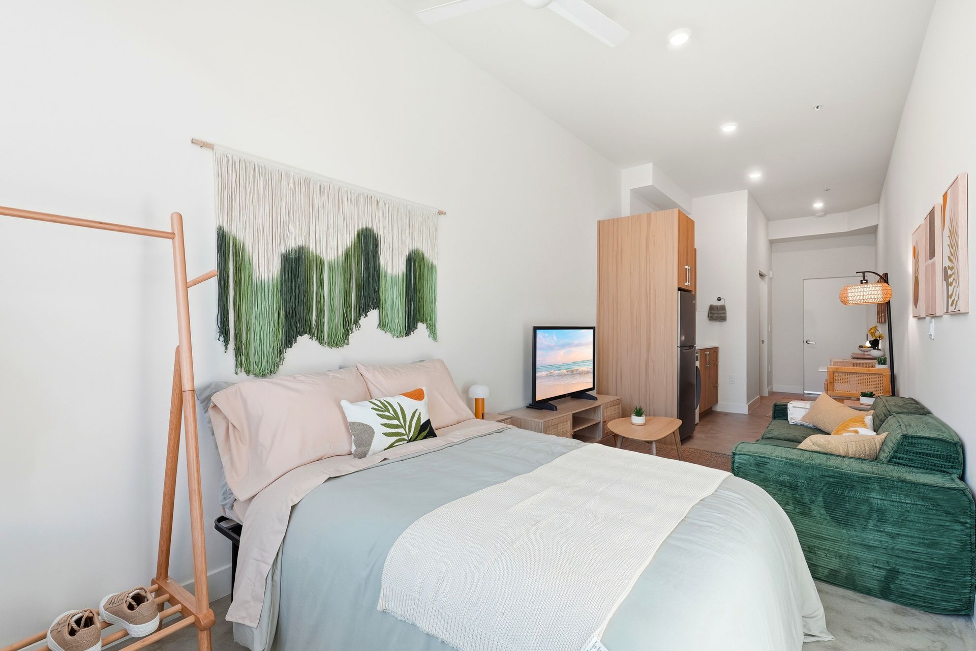 Bedroom with bed, macrame wall hanging, TV, small sofa, and clothing rack.