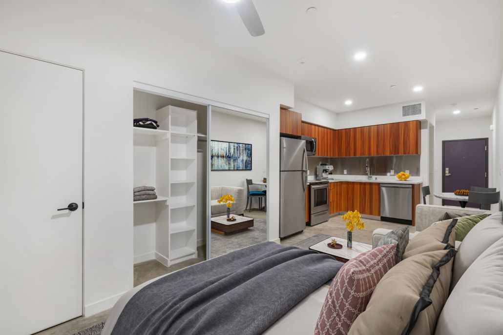 A bedroom with a bed and a kitchen in the background