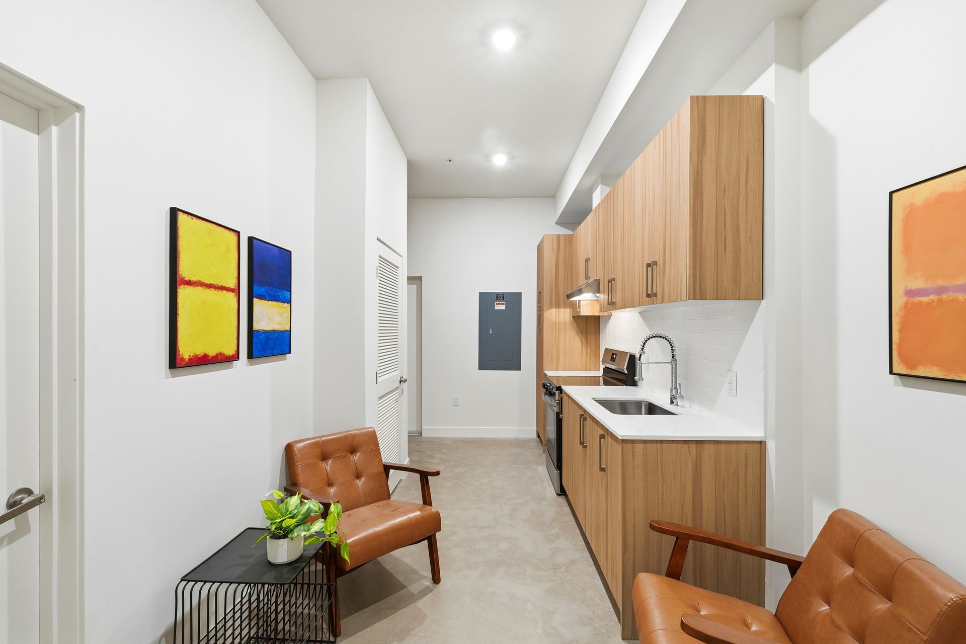 Hallway with seating and kitchenette; wooden cabinets, art on walls, tan leather chairs.