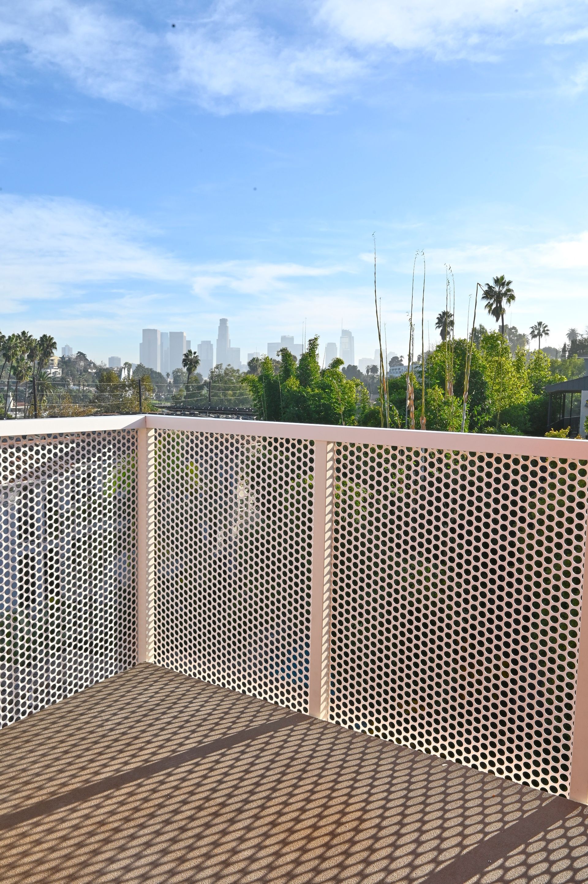 Balcony with patterned white railing overlooking a city skyline under a blue sky.