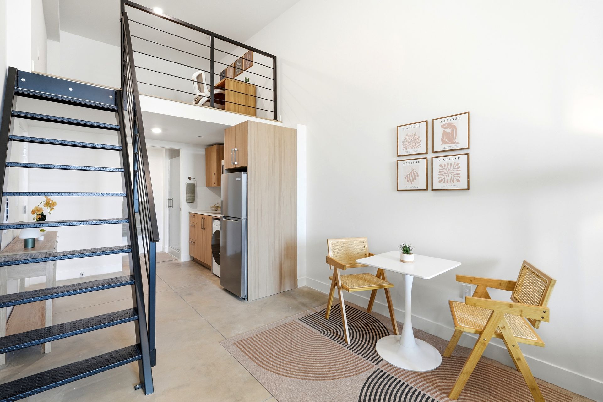 Bright loft dining area with staircase, white table, wooden chairs, and small kitchen nook