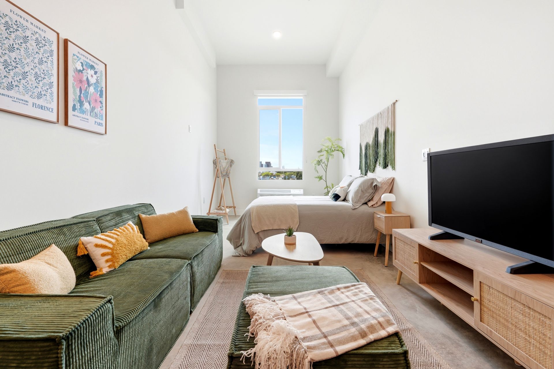 Bright modern living room with green sofa, beige armchair, TV, and large window.