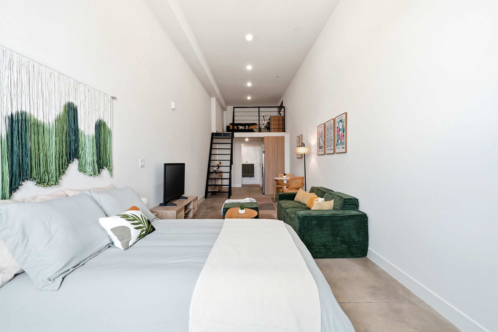 Bright modern studio bedroom with white bed, green accents, sofa, and a lofted mezzanine at the back