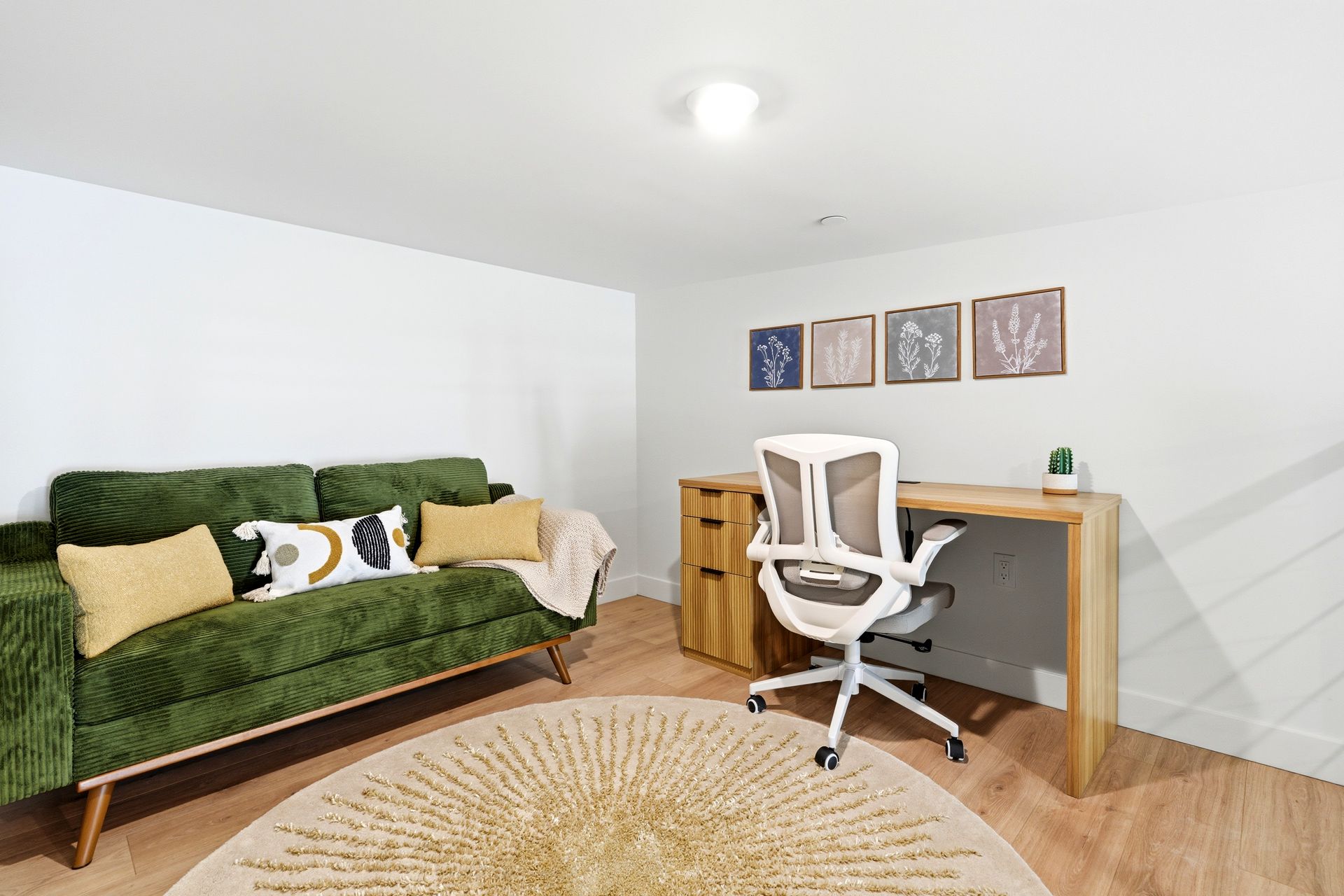 Bright home office with green sofa, desk, white chair, wall art, and round rug