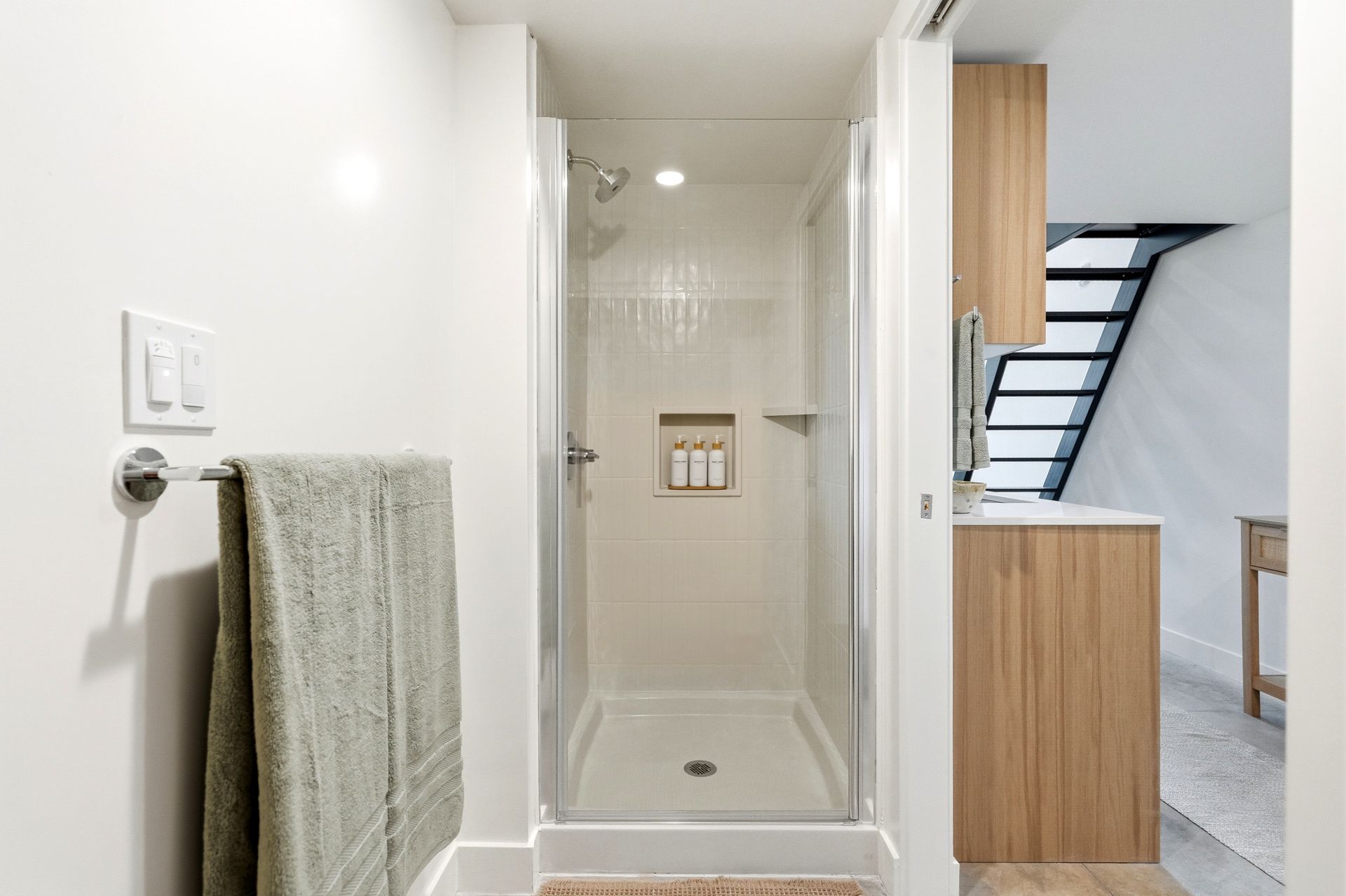 Bathroom with glass shower stall, towel on wall, and hallway view to staircase and wood cabinet