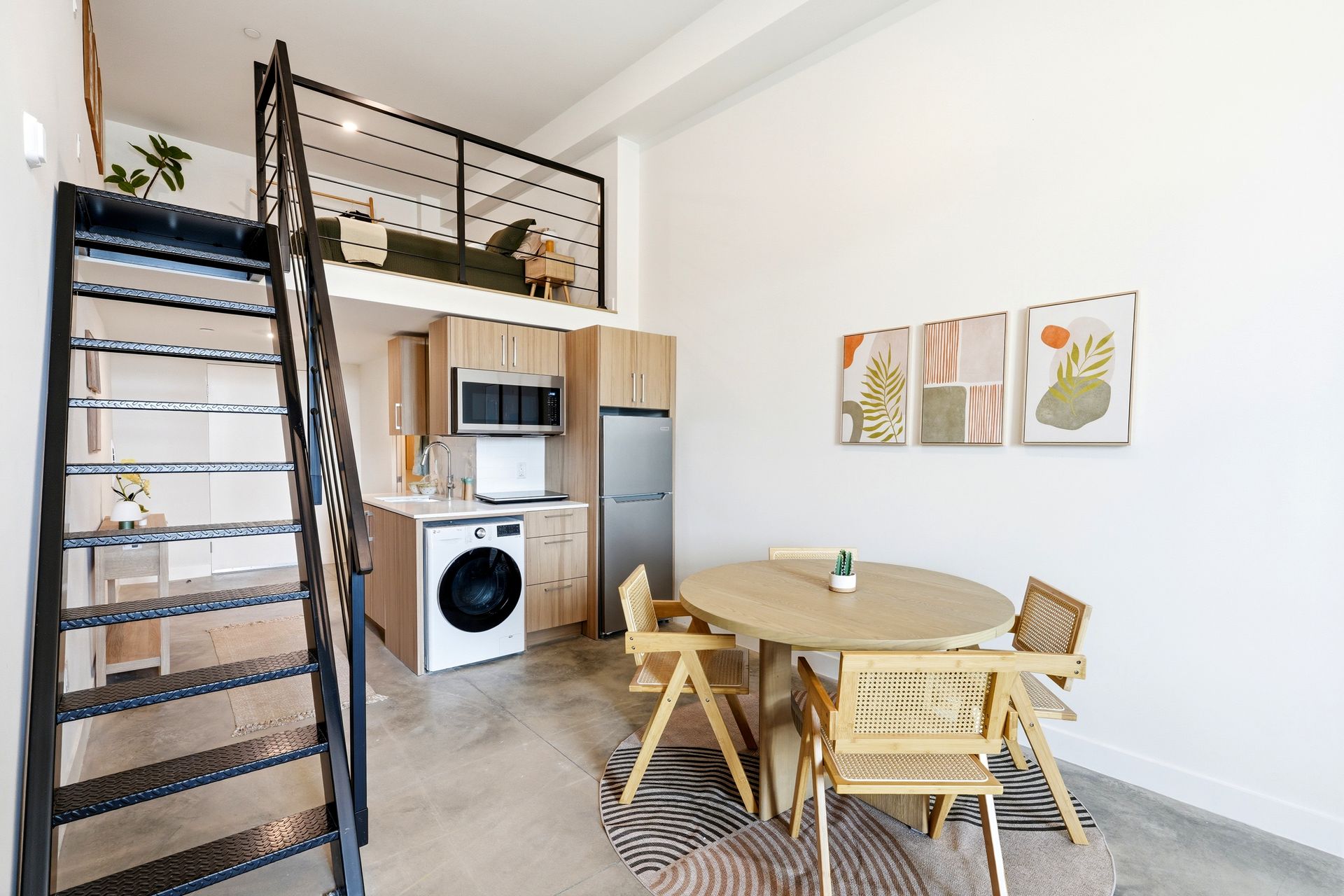 Small loft dining area with round table, wicker chairs, ladder stairs, and compact kitchen nook