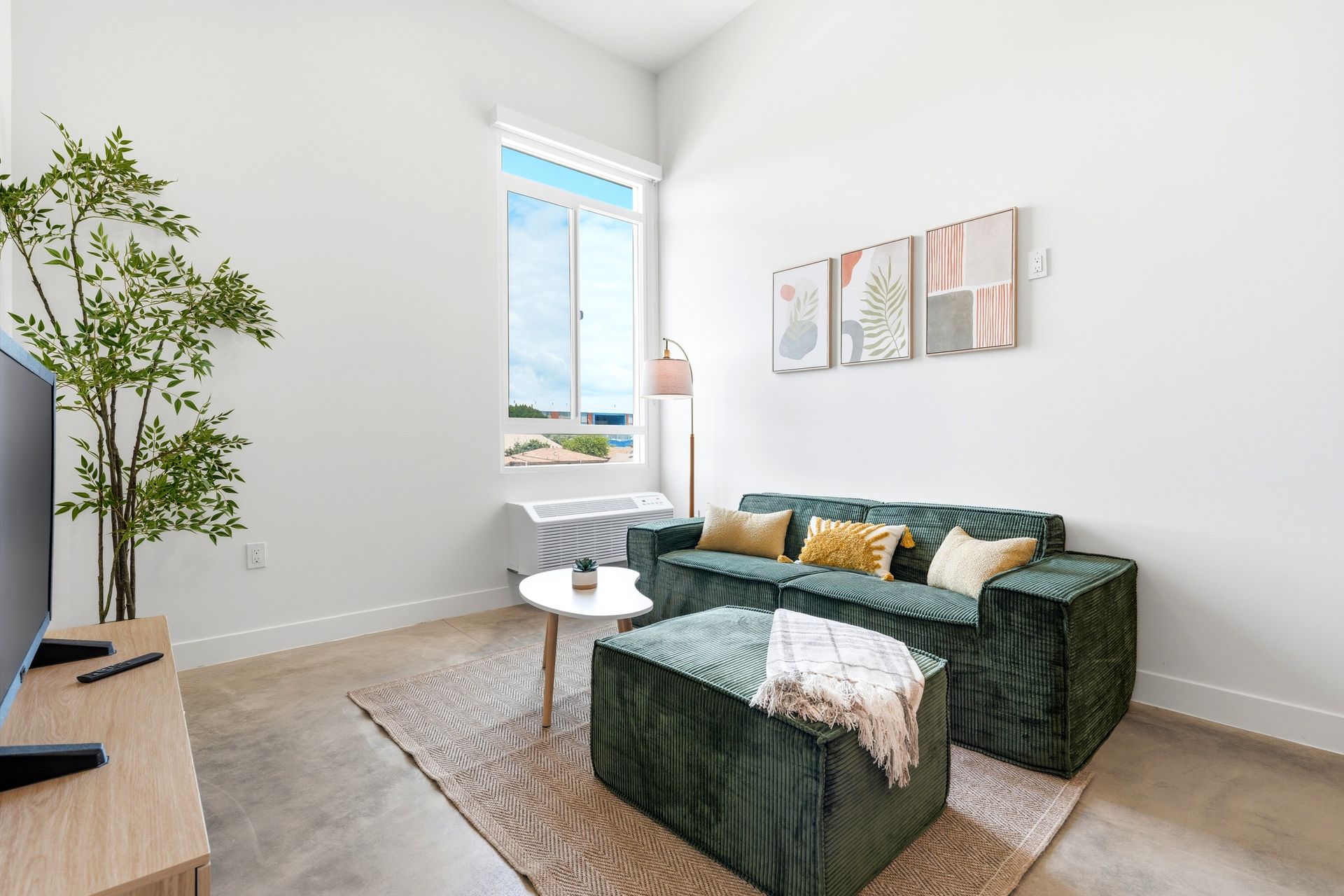 Bright modern living room with green sofa, ottoman, window, and wall art