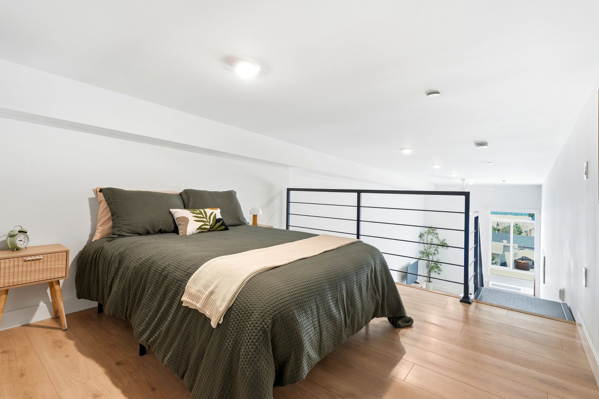 Bright bedroom with a large bed, wood floor, and black railing overlooking a lower level