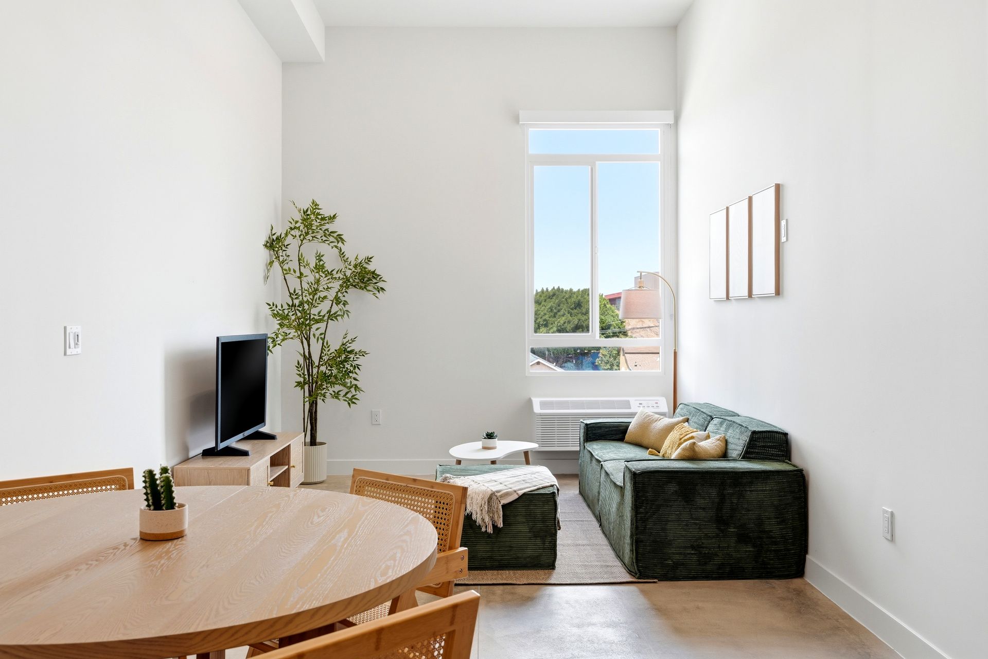 Minimalist living room with green sofa, round wooden table, TV, and bright window